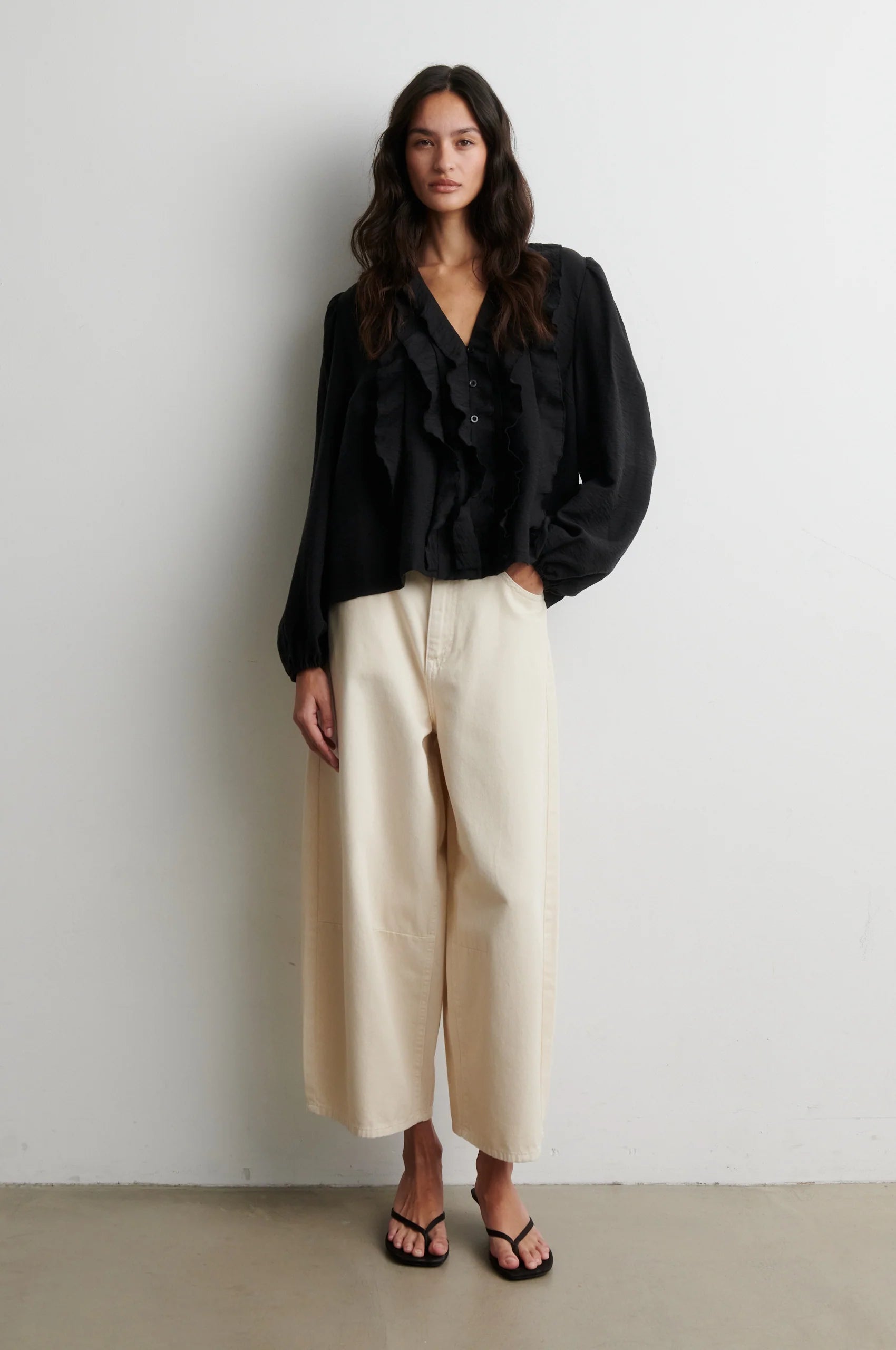 Second Female Rayna black ruffle v neck blouse styled with cream wide-leg trousers Second Female Rayna black ruffle blouse styled with cream wide-leg trousers